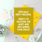 Empty Nester Card by SixElevenCreations. A yellow greeting card with a geometric pattern and white text reading 'OFFICIALLY EMPTY NESTERS. HERE'S TO ENJOYING THE QUIET AND RECLAIMING YOUR SPACE!' shown with a solid yellow envelope on a light yellow background. Product Code SE1403A6