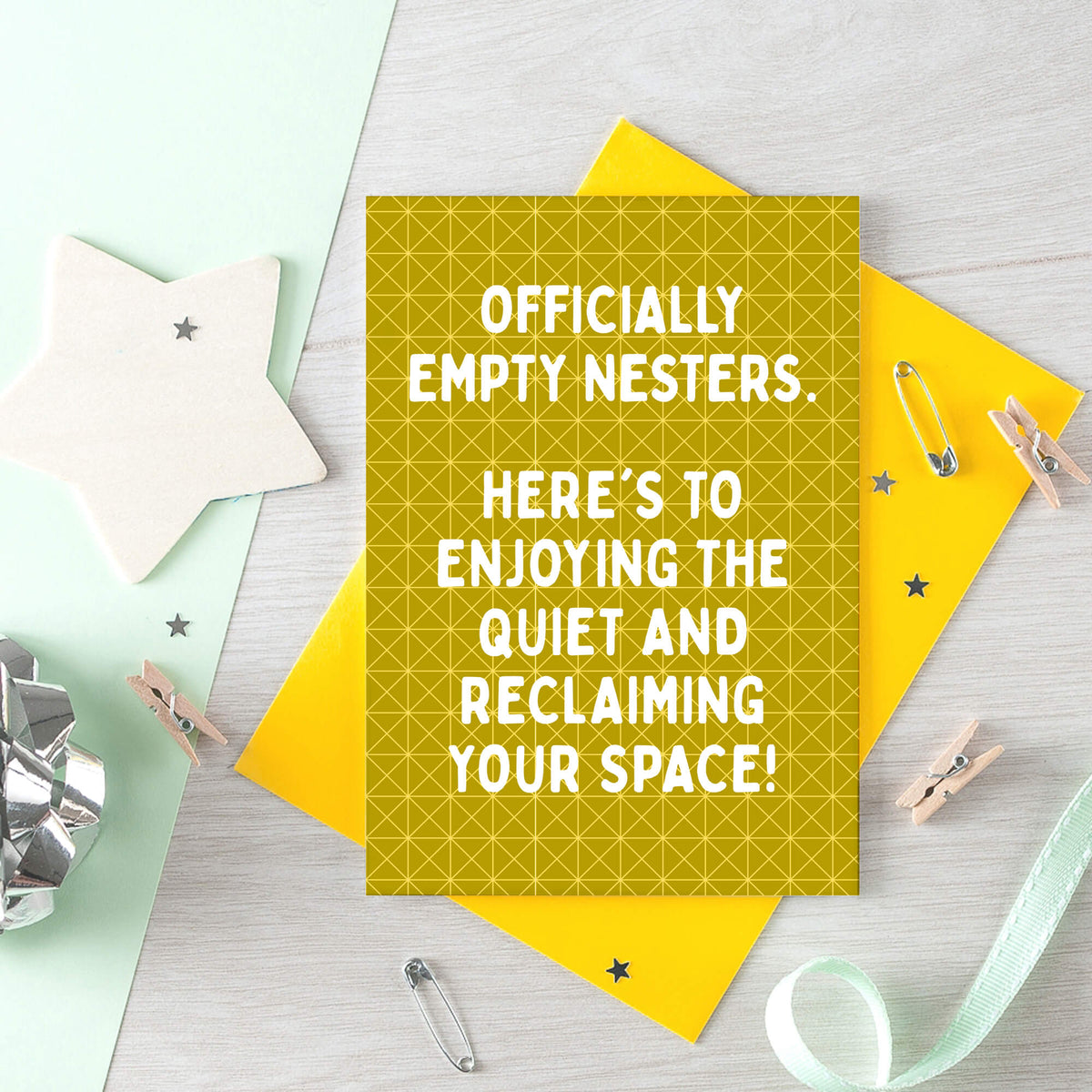 Empty Nester Card by SixElevenCreations. A yellow greeting card with a geometric pattern and white text reading 'OFFICIALLY EMPTY NESTERS. HERE'S TO ENJOYING THE QUIET AND RECLAIMING YOUR SPACE!' shown with a solid yellow envelope on a light yellow background. Product Code SE1403A6